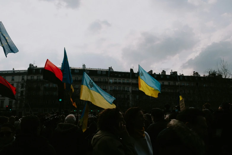 several flags are displayed at a gathering on the sidewalk