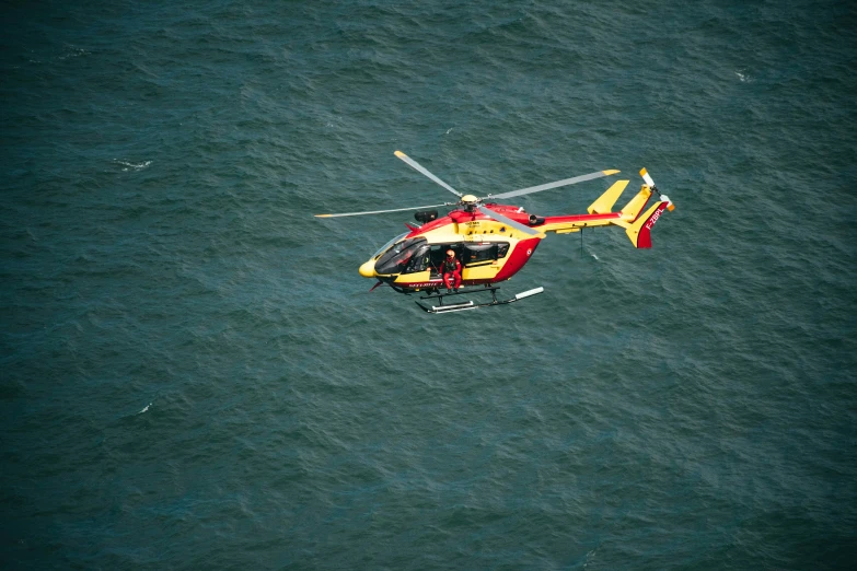 a helicopter with a red front flies above the water