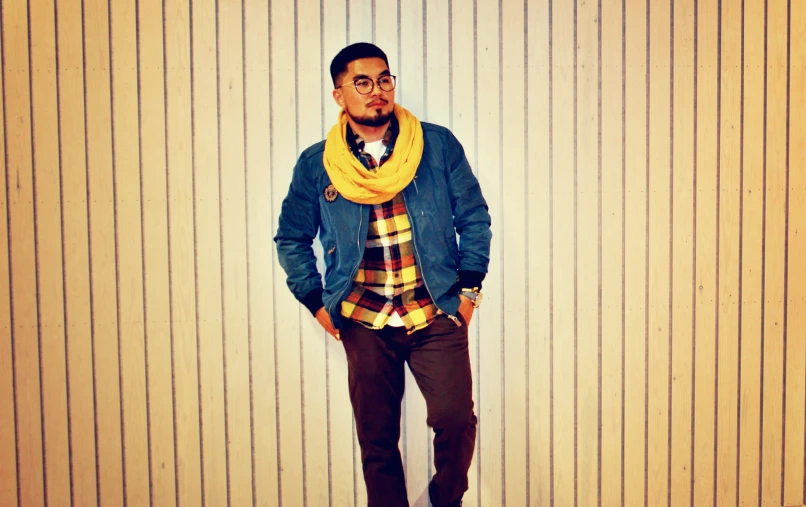 a man in yellow scarf standing next to a wooden wall