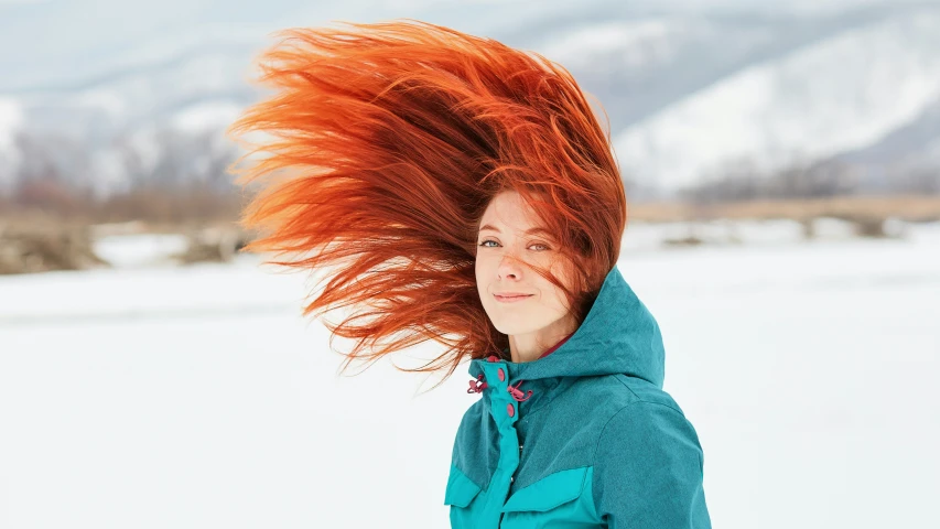 a woman is smiling while she has her red hair blowing