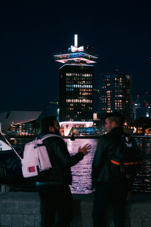 two young men standing next to the water looking at their cellphones