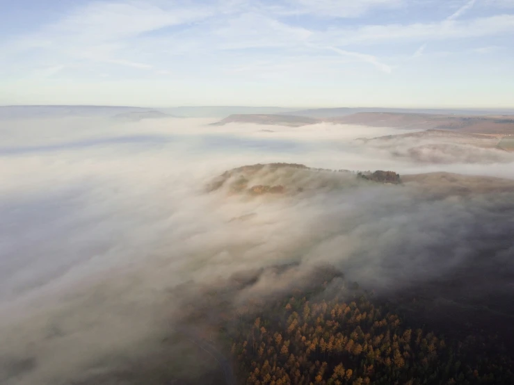 a foggy landscape with trees and some clouds