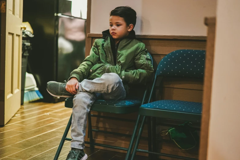 the boy sitting on the green chair has a brown and black hat