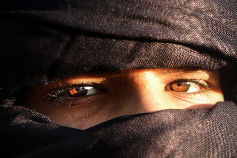 person with hooded cloak and eye looking at camera