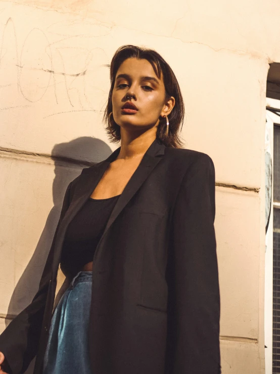 a woman standing by the side of a building with a black jacket and a blue skirt