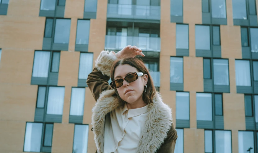 a woman in a fur jacket and sunglasses stands in front of a building