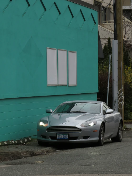 the silver sports car is parked next to the building