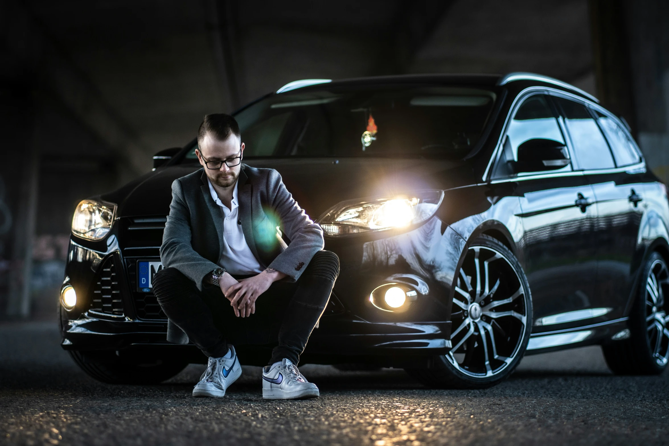 a man wearing glasses is sitting on the front of his black car
