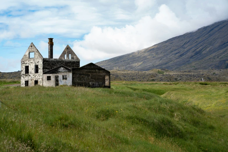 the old barn is in the middle of a field with mountains in the background