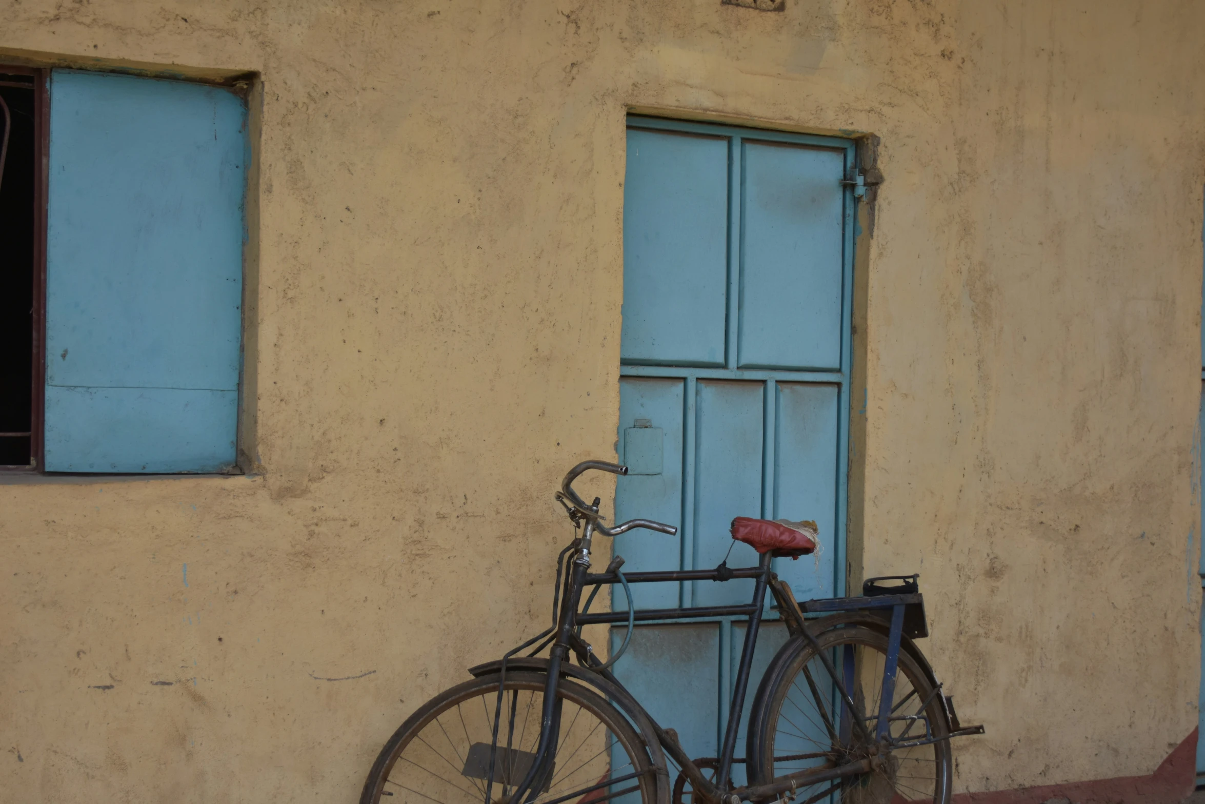 the bicycle is parked against a yellow wall with two blue windows