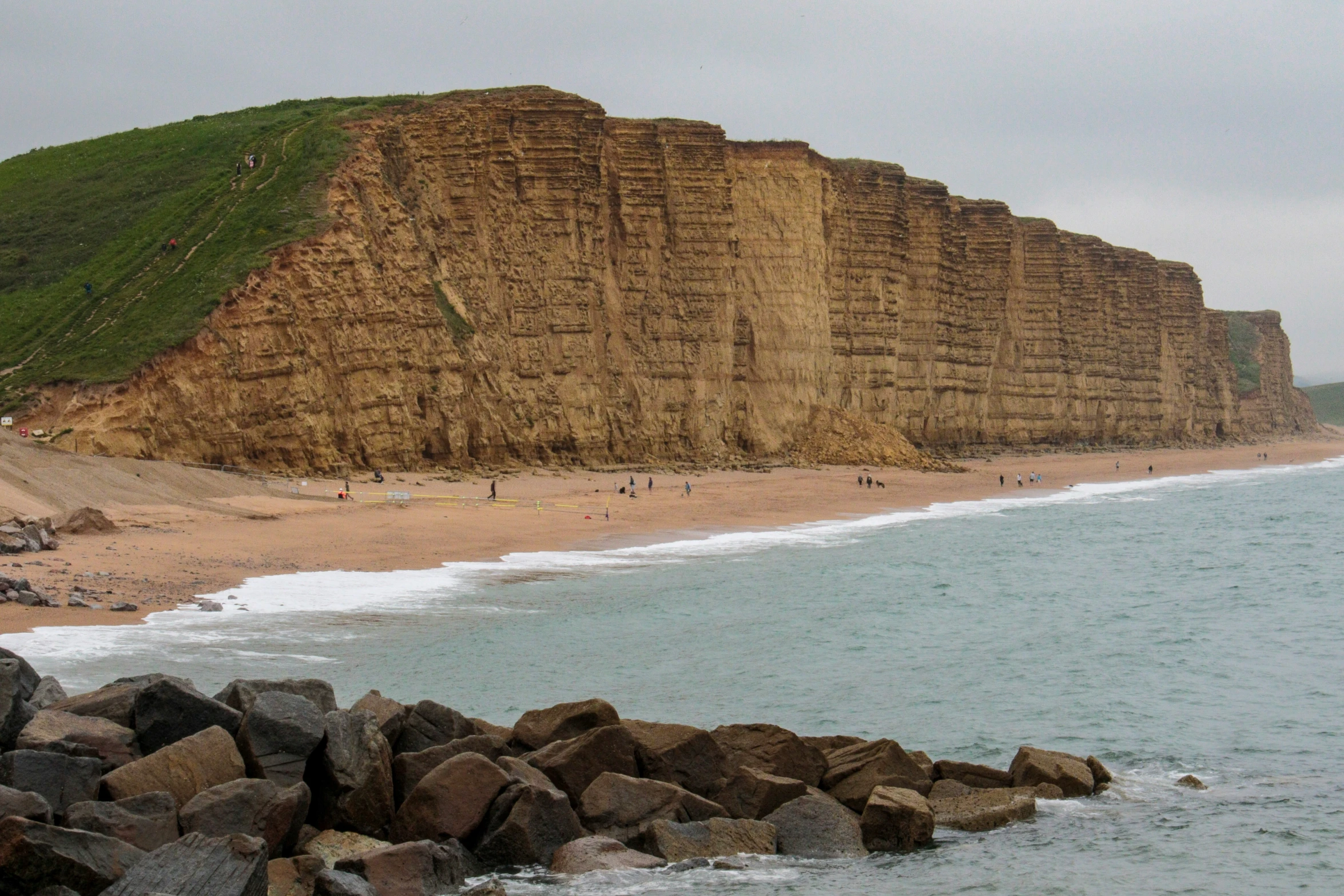 people playing in the water on a beach next to rocky cliff