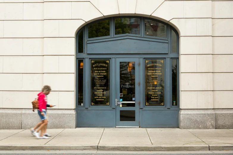 a woman walking on a city sidewalk past a restaurant