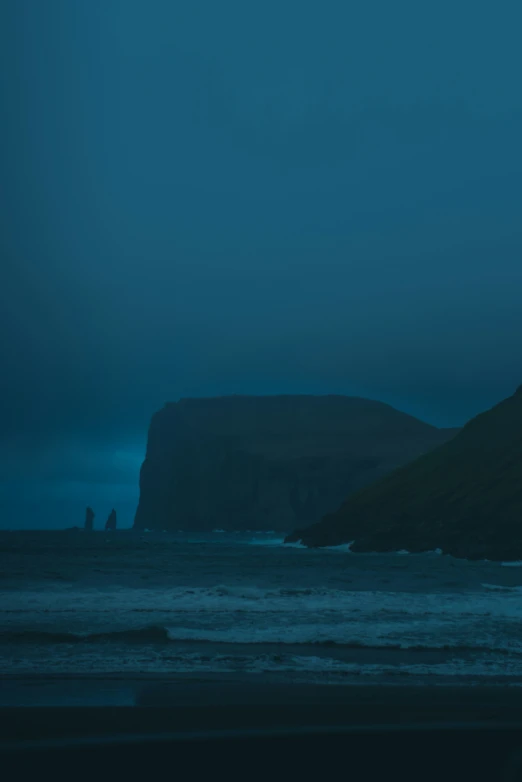 an empty beach on a rainy day with one person standing at the ocean