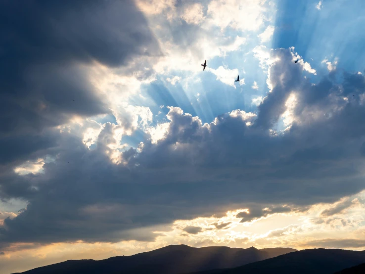 two birds flying in the clouds above some mountains