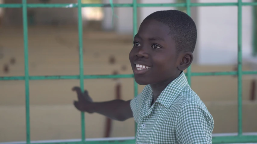 a boy standing with his hand up in front of a gate