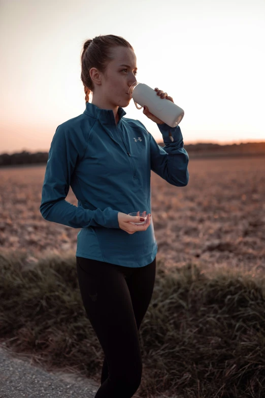 woman drinking from a bottle while running along a trail