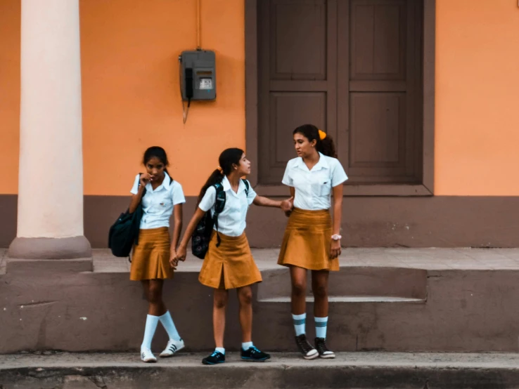 three girls in skirts and white shirts talking to each other