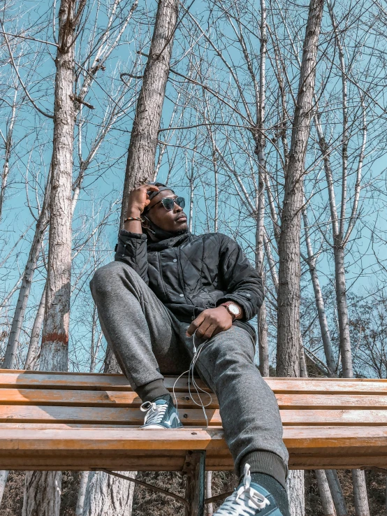 a young black man wearing a jacket and sunglasses sitting on a bench