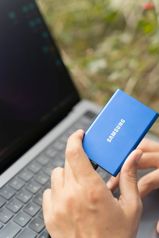 person with blue cellphone sitting in front of laptop computer