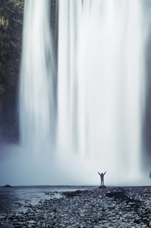 a person is standing in front of a waterfall with their arms spread open