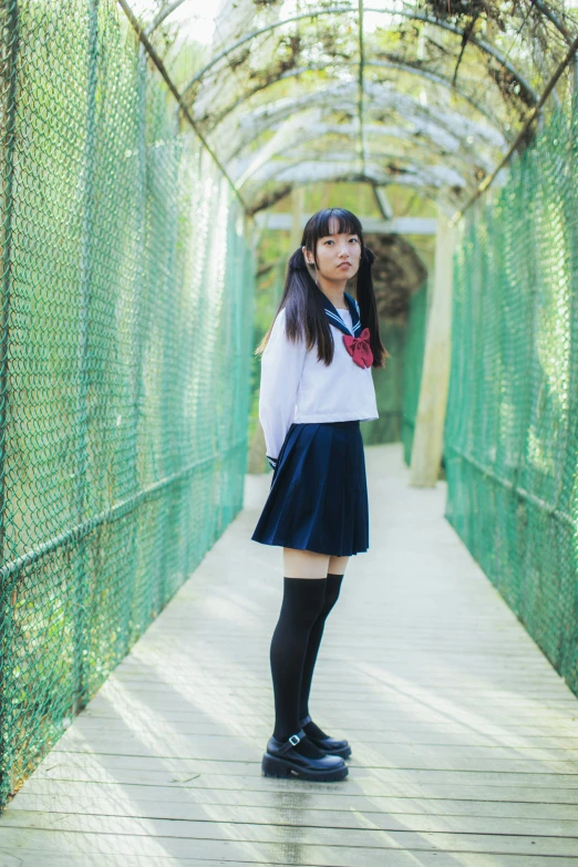 a young asian woman wearing knee high black boots is standing in a long covered bridge