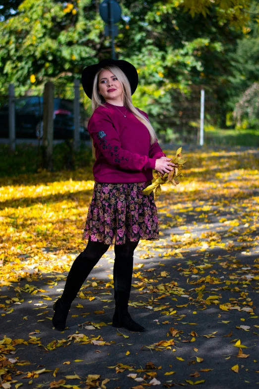 the woman poses with her hat on while in the leaves