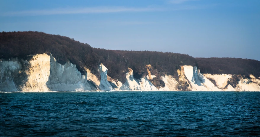 large rocks on the shoreline with trees on the hill