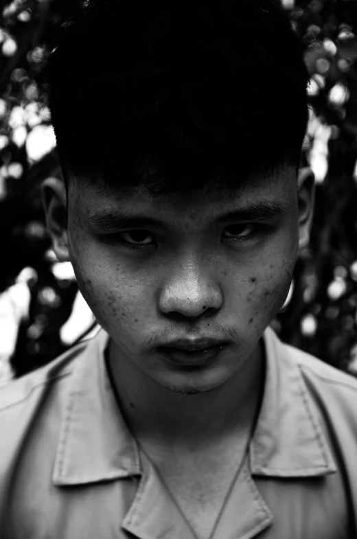 a boy with black hair is standing in front of a tree