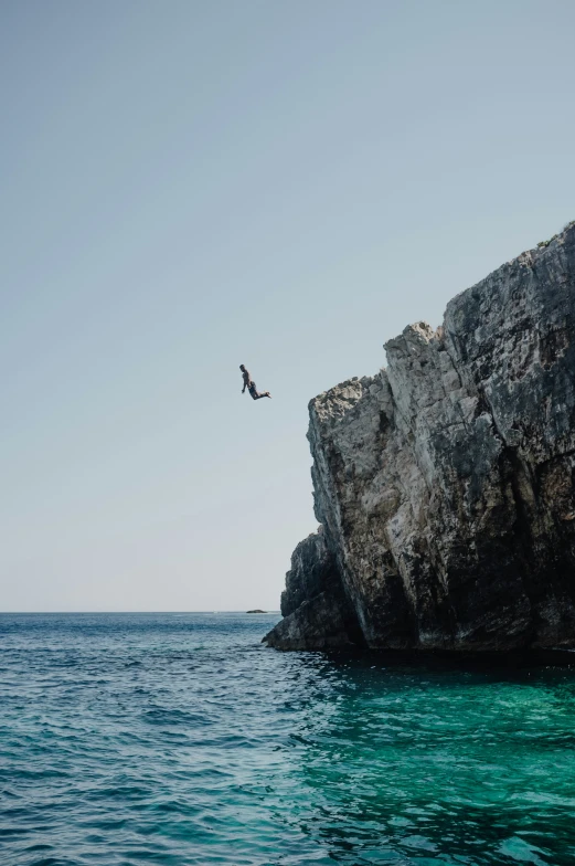 bird flies over the ocean next to a rock formation