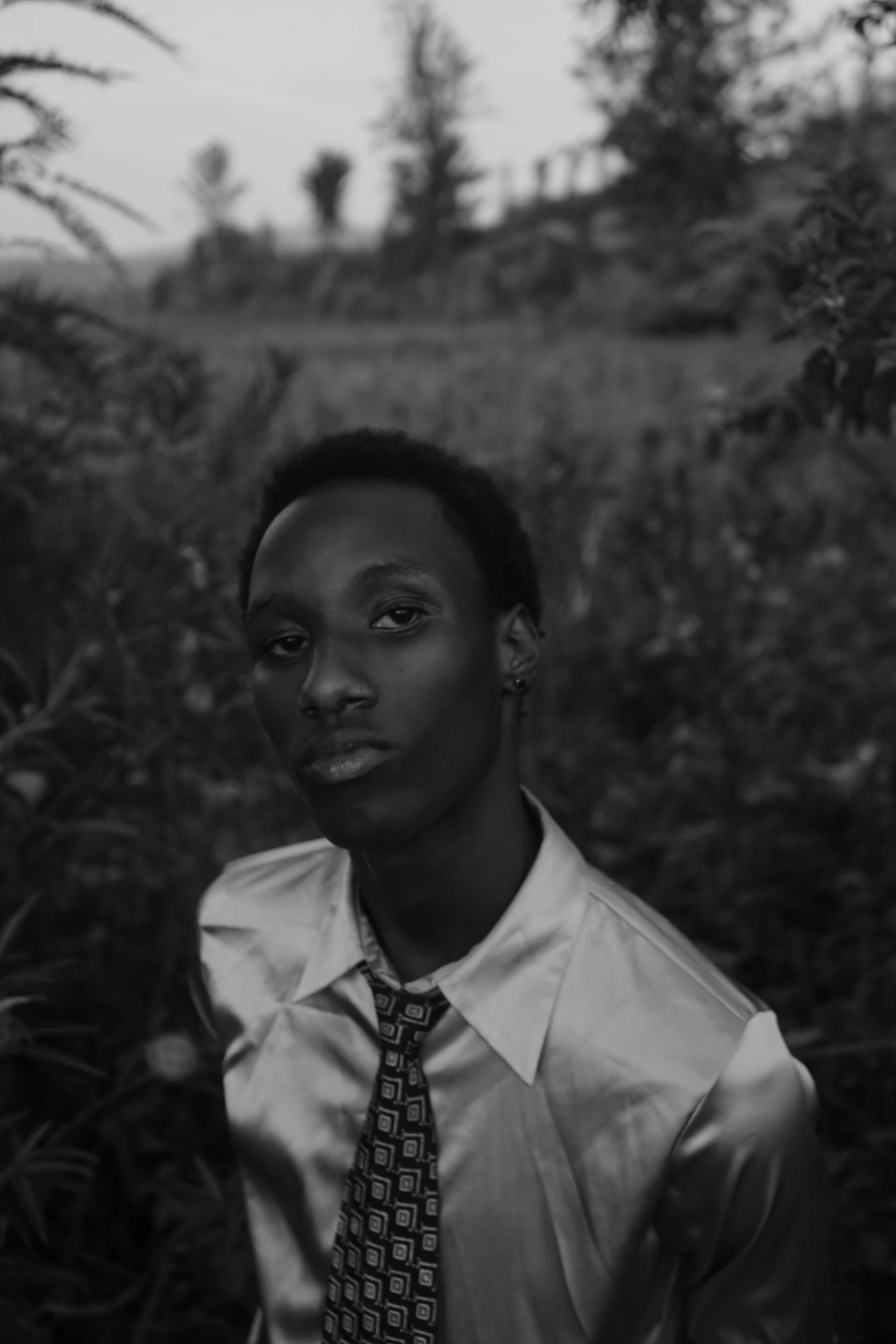 a young man in a tie stands in a grassy field