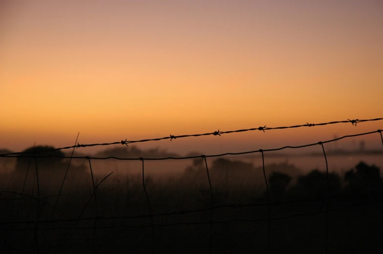 a long barbed wire fence is shown with the sun setting in the background