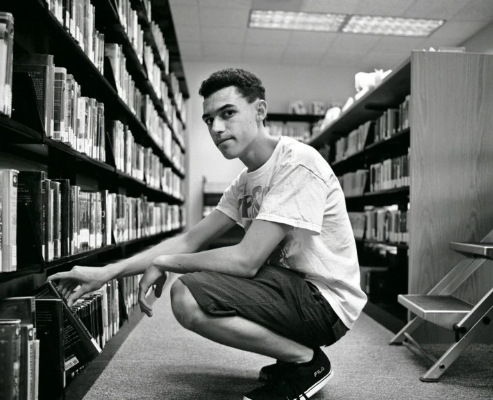 a young man squatting in front of books in a liry