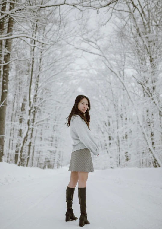 a young woman standing in the snow near trees