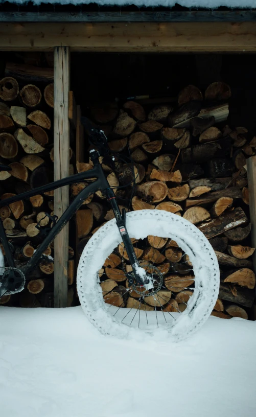 a bike is standing next to logs in the snow