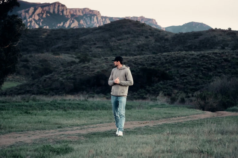 man walking in grassy field next to a mountain