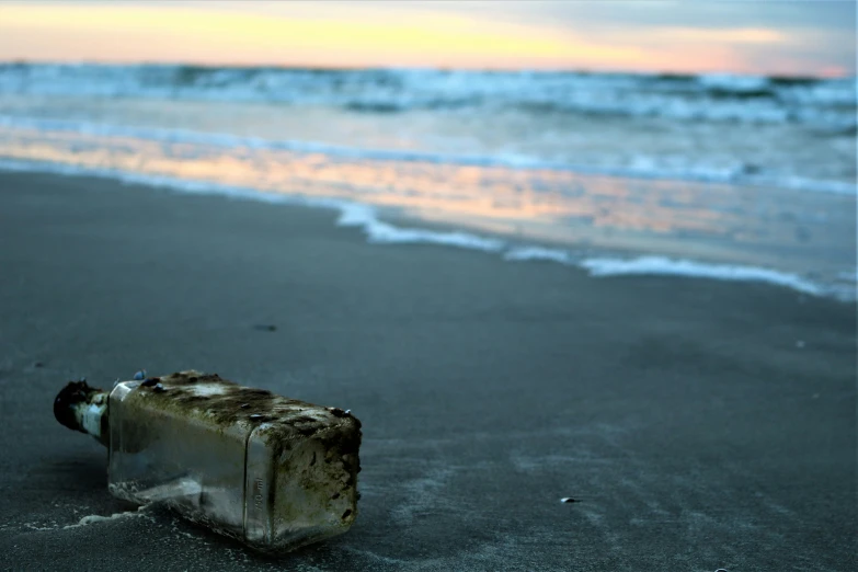 a dirty bottle on the beach next to water