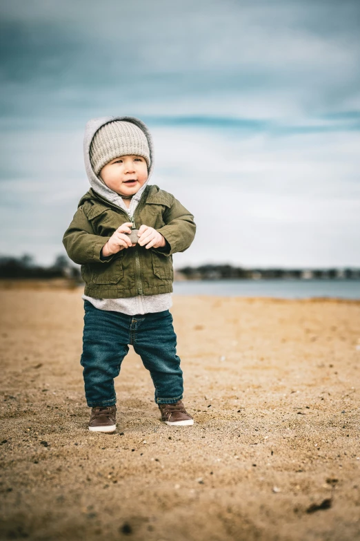 young toddler standing on the beach holding his hands together