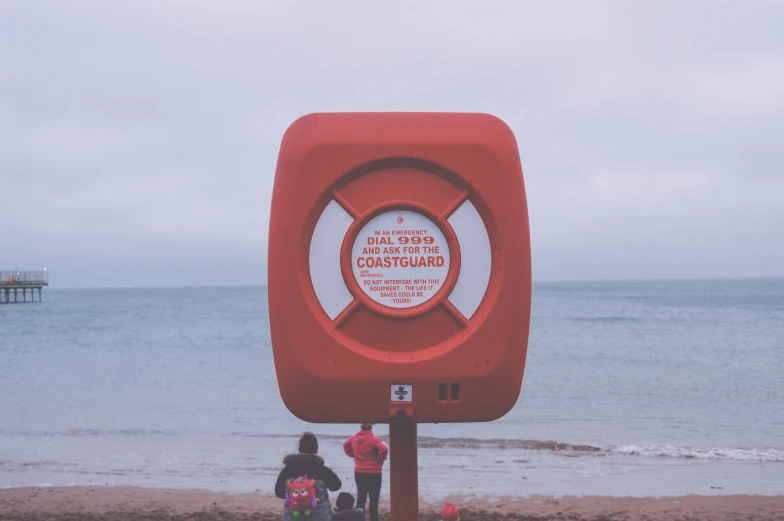 people are standing around the red sculpture on the beach