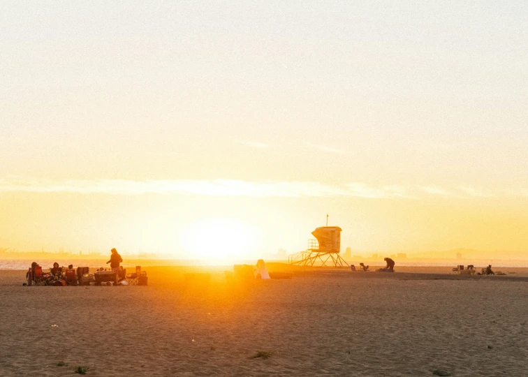 people gather on the beach at sunset with lifeguard tower