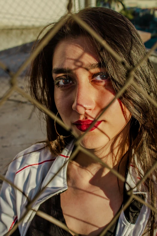 a woman standing behind a fence while wearing makeup