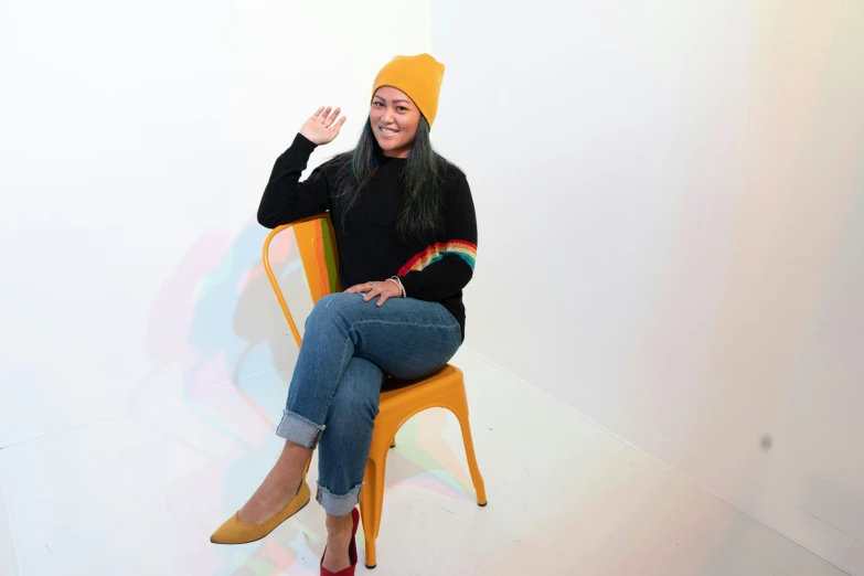 the smiling girl in a knitted hat is sitting on an orange chair
