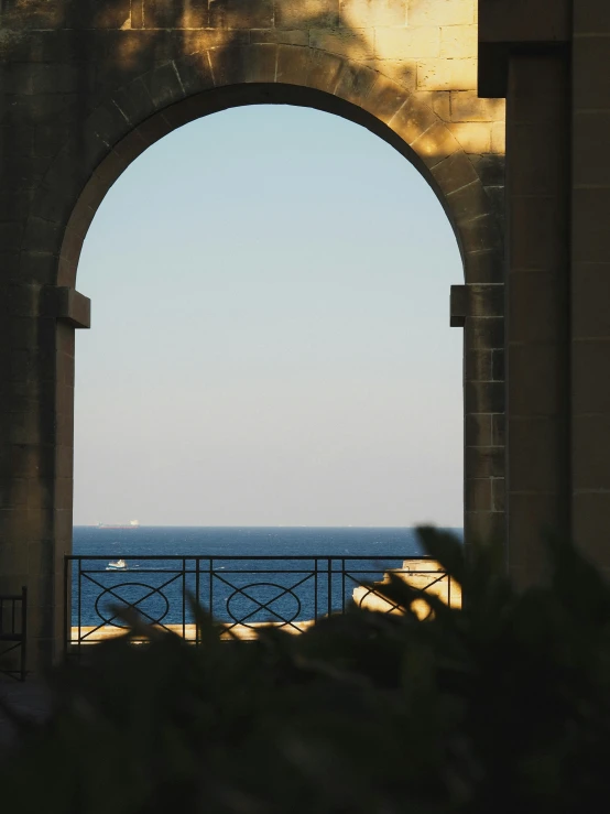 the light is shining on a blue ocean seen through an arched stone archway