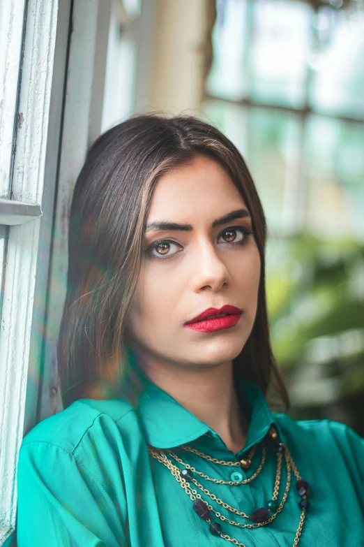 the woman is looking out a window and is wearing green