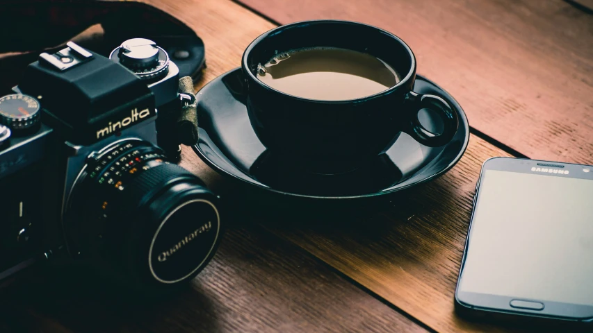 camera and coffee cup on a table with an extra lens