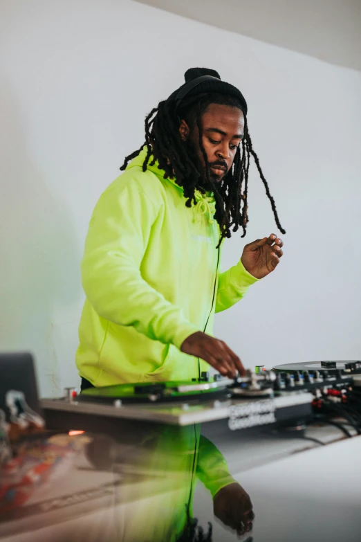 a man in a neon yellow jacket stands behind a dj's equipment