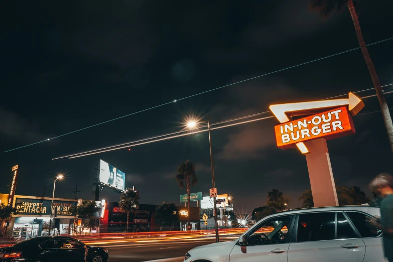 a parking lot filled with lots of traffic next to a tall neon sign