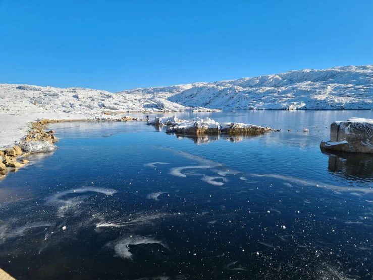 snow is laying on the ground by the water