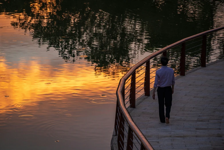 man walking along a river at sunset