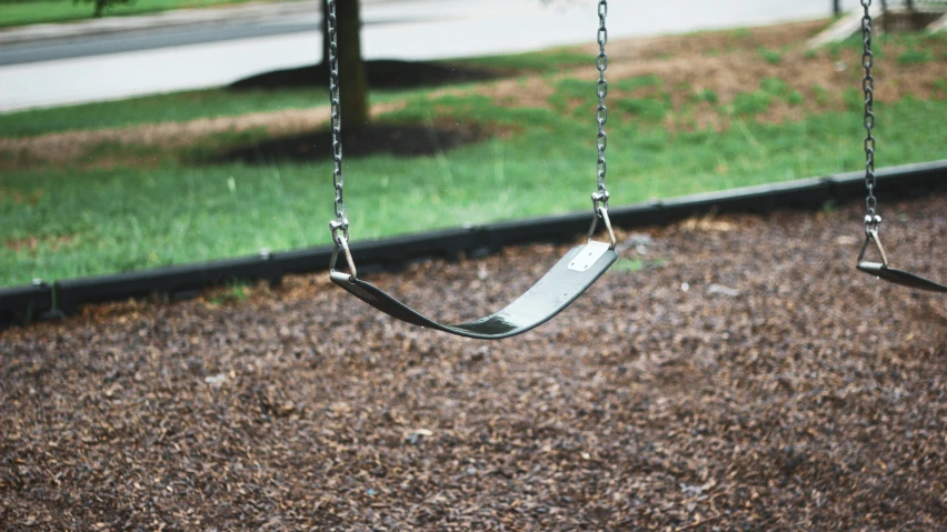 a wooden swing in a park with brown gravel