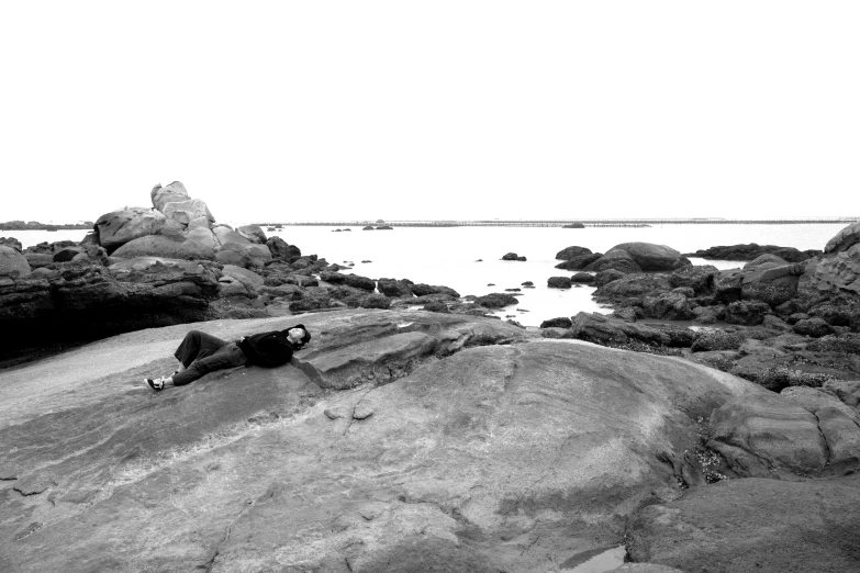 a man laying on top of a large rock next to the ocean